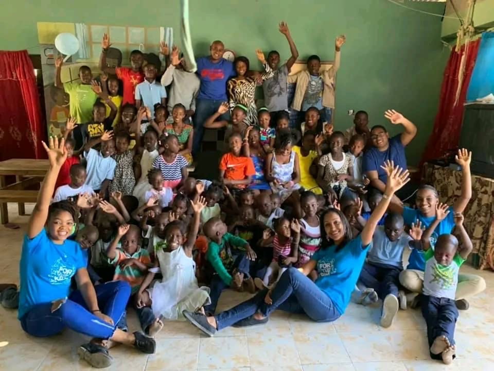 Groupe d'enfants et d'adultes en salle de classe, souriant et levant la main