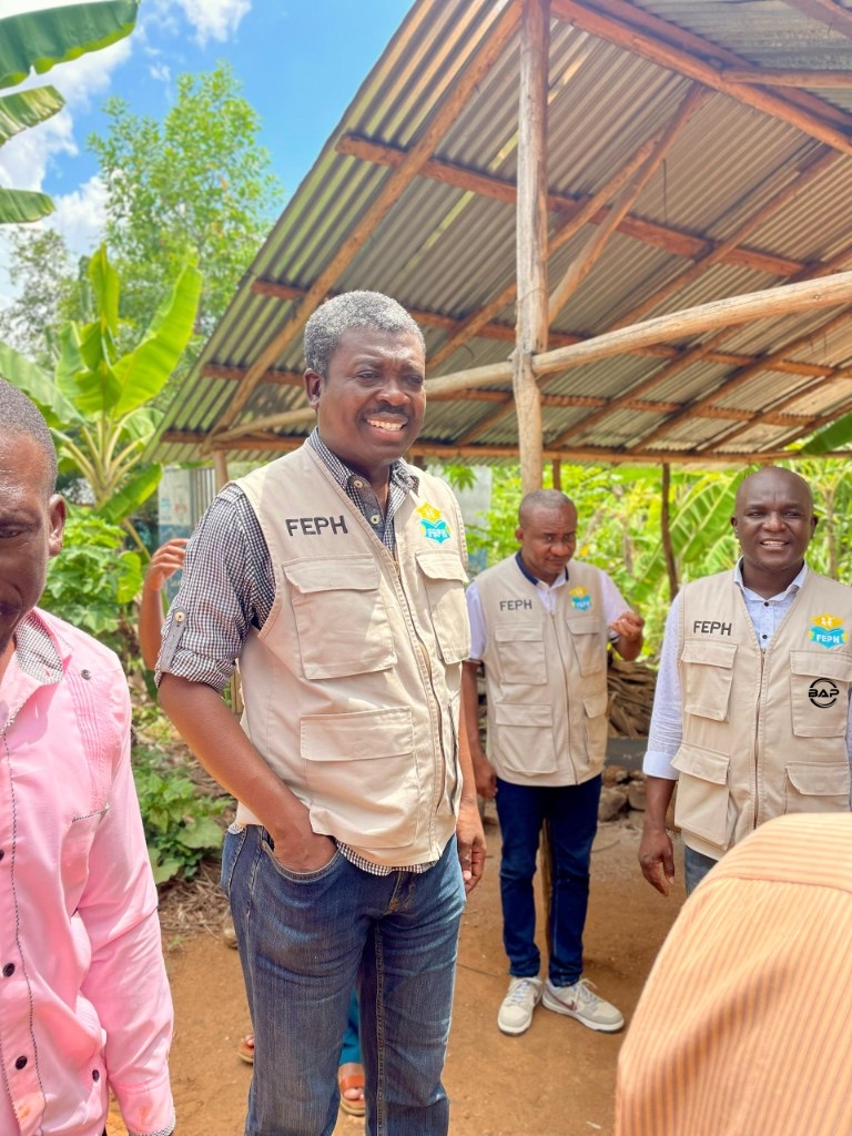 Sur le terrain : agents en gilet FEPH devant une structure en tôle, végétation tropicale et ciel bleu
